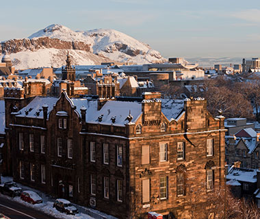View across old Edinburgh from Castle Esplanade to Aurthurs Seat, blanketed in snow in the morning sun